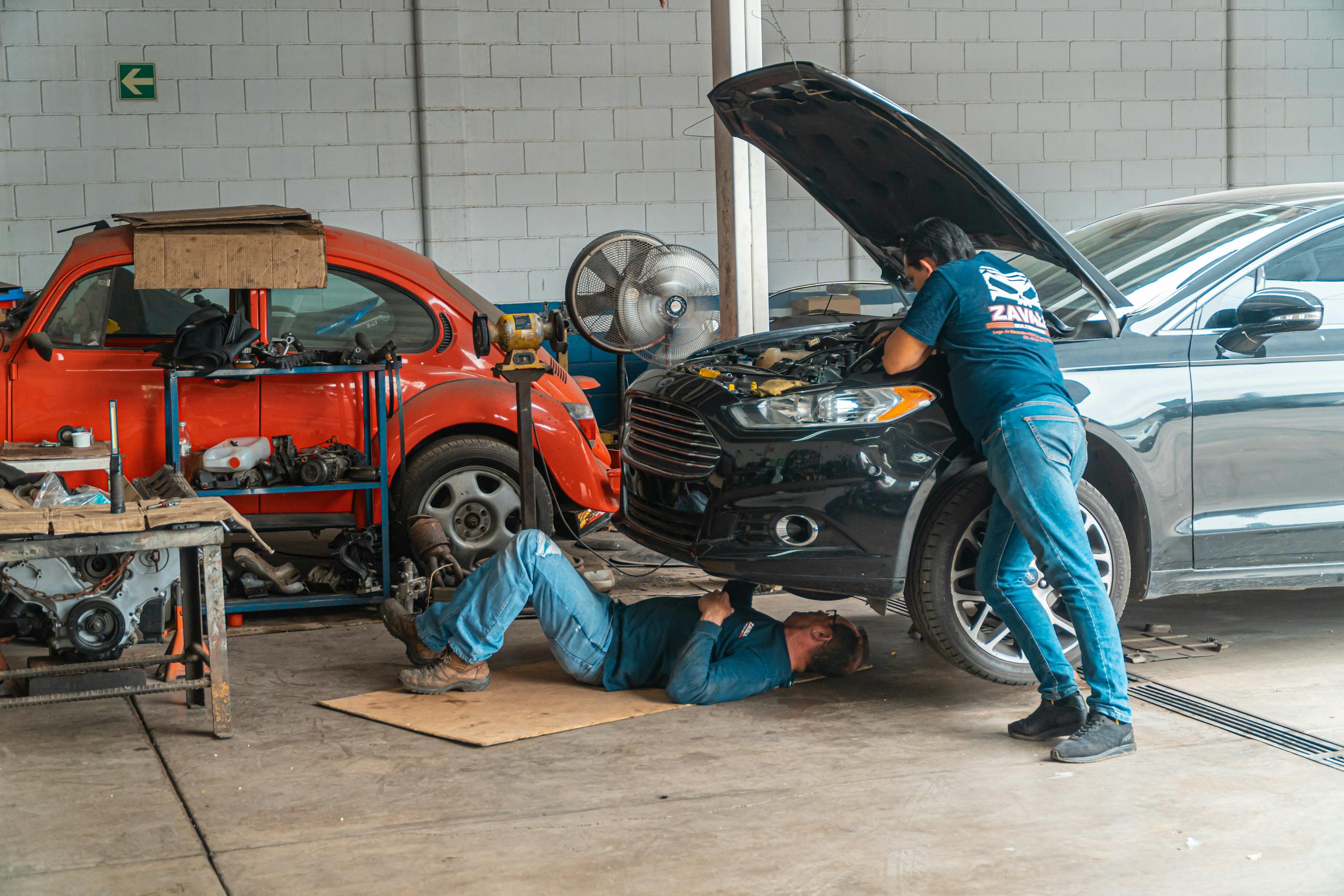 Mechanics working in an automotive workshop, repairing cars and performing mechanical maintenance.